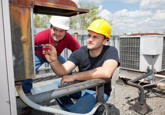 Two HVAC technicians servicing a rooftop air conditioning unit
